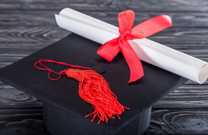 Graduation hat and diploma with red ribbon on wooden table Graduation hat and diploma with red ribbon on wooden table