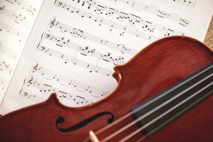 In love with classic music. Close up view of brown violin lying on music score sheet. Violin lessons